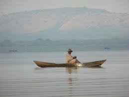 Traveler in wooden boat on calm Rwandan lake with mountain backdrop and mirror-like water reflection BY RWACU TOURS.